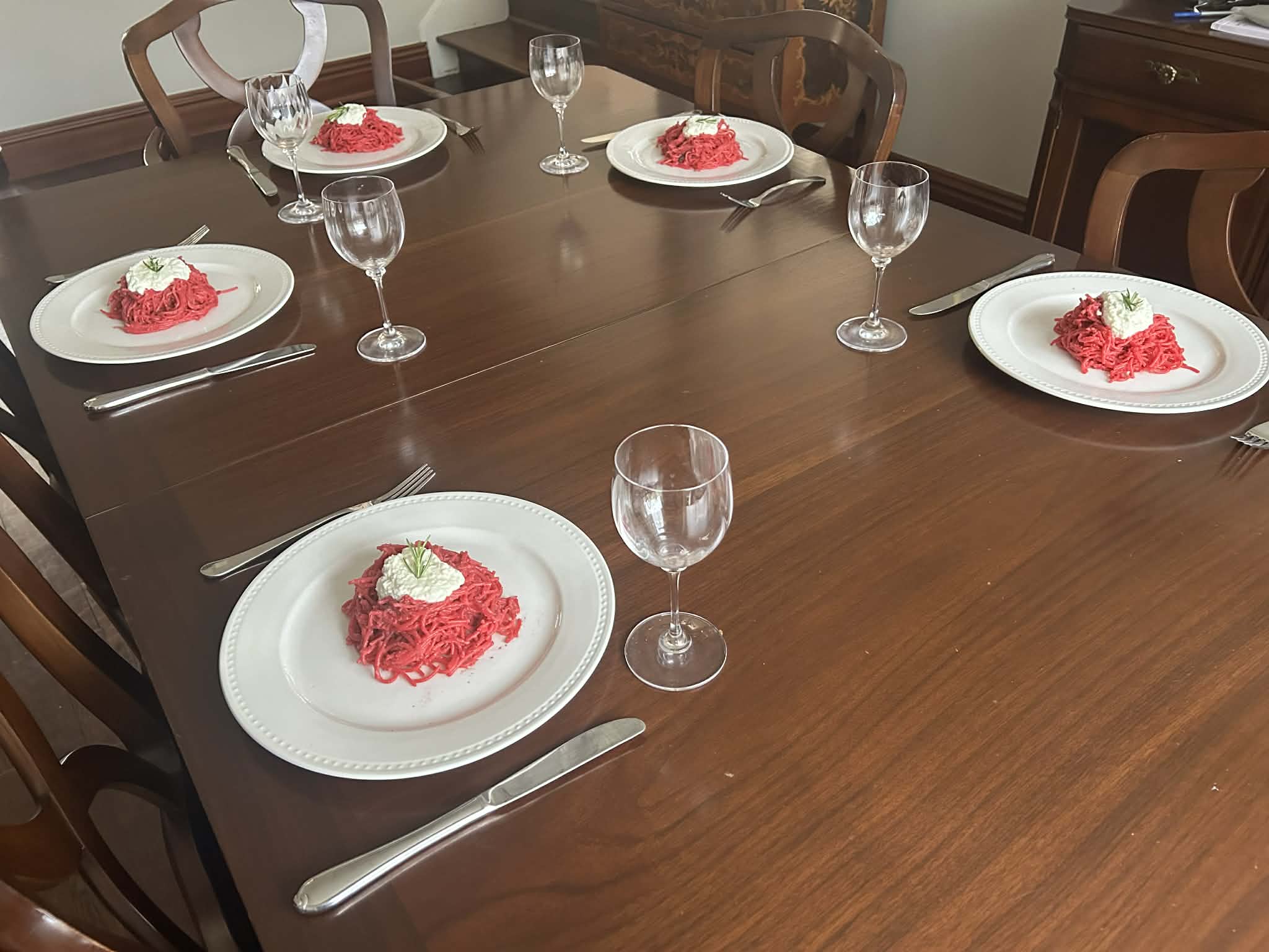 A full dinner table set with beet pasta courses at every place setting