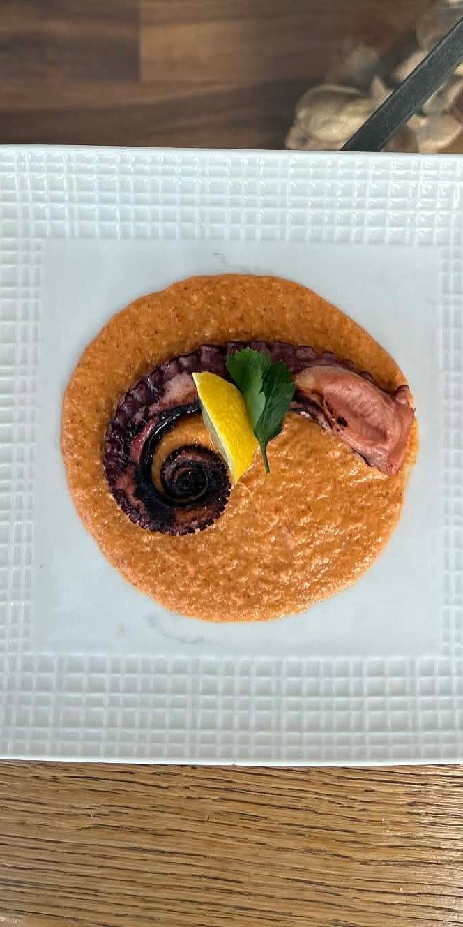 A private dinner table set with a plated octopus course