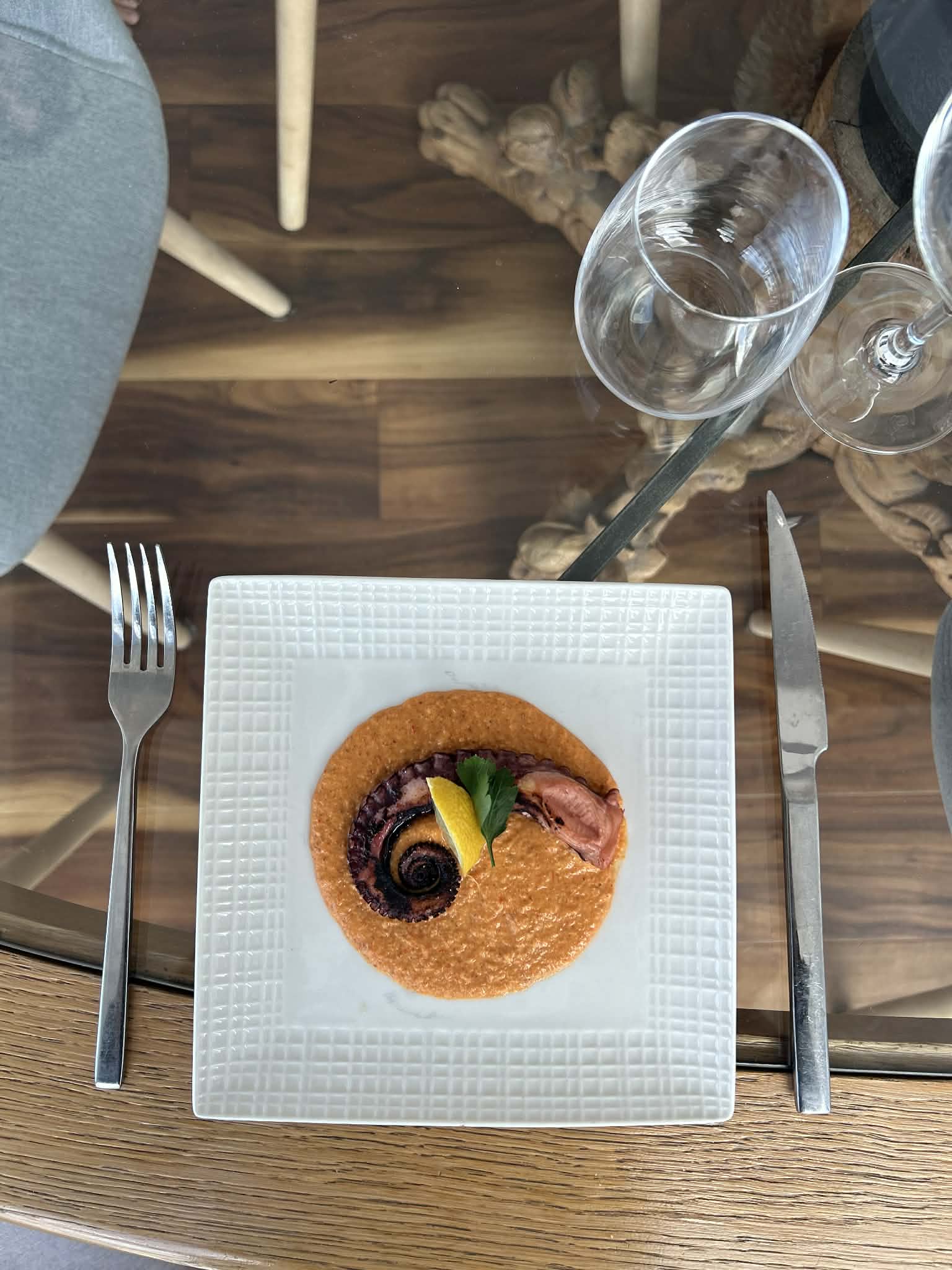 A private dinner table set with wine glasses and a plated octopus course
